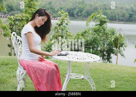 Giovani asiatici donna incinta piani il budget familiare con la calcolatrice. bellissima femmina calcolando la sua bollette domestiche in giardino Foto Stock