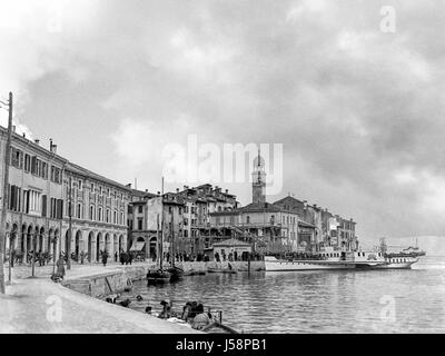 I passeggeri scendono dalla PS Baldo, un battello a vapore in un ignoto porta sul Lago di Garda, Italia nel 1909. Un certo numero di piccole imbarcazioni e due grandi barche a vela sono ormeggiate nel porto. Sul lato del porto una chiesa ha un ponteggio intorno ad esso e sta subendo alcuni restauro, In basso al centro sulla fotografia di un gruppo di donne sono il lavaggio della biancheria nel lago. Ripristinato utilizzando una scansione ad alta risoluzione prese dal negativo originale. Foto Stock