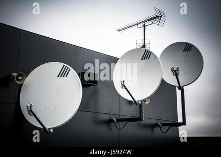 Trio di antenne paraboliche attaccata alla parete alta sulla costruzione Foto Stock