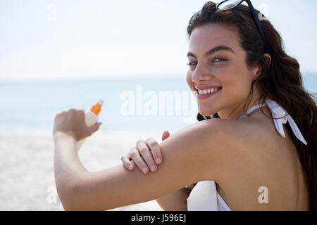 Ritratto di donna sorridente applicando sunscream su bracci a beach Foto Stock