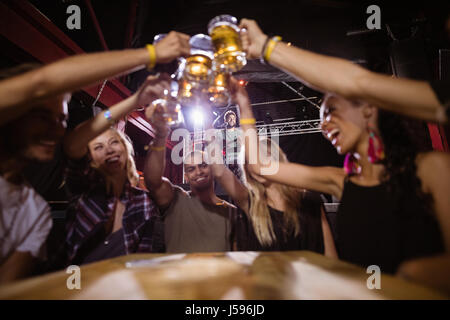 Happy amici tostare bicchieri da birra seduti a tavola nel club Foto Stock