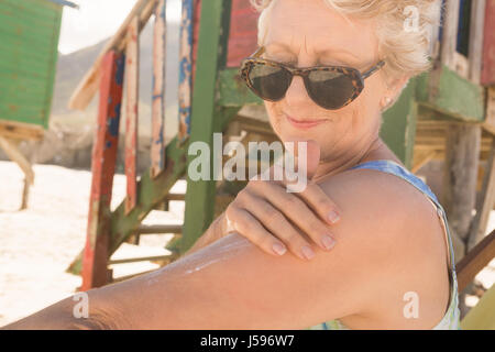 Close up della donna di applicare una lozione solare mentre in piedi contro la capanna a spiaggia Foto Stock