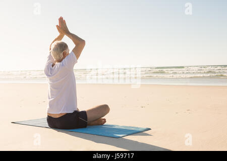 Senior uomo con braccia alzate meditando a beach Foto Stock