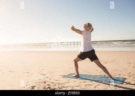 Attivo uomo senior a praticare yoga in spiaggia Foto Stock