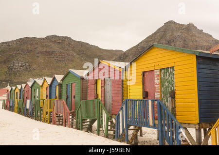 Variopinte cabine in legno sulla sabbia contro la montagna Foto Stock