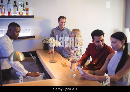 Due coppie interagenti con ciascun altro mentre è seduto al banco bar nel ristorante Foto Stock