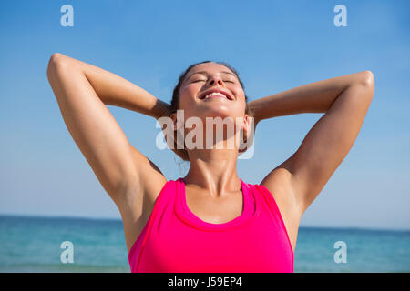 Sorridente giovane donna con gli occhi chiusi gli esercizi in spiaggia sulla giornata di sole Foto Stock