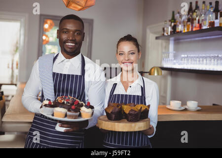 Ritratto di sorridente cameriere e cameriera holding dessert al contatore nel ristorante Foto Stock