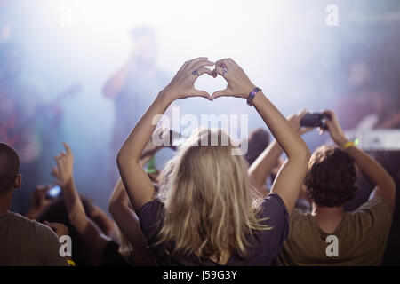 Vista posteriore della donna messa a forma di cuore mentre godendo al nightclub durante il festival di musica Foto Stock