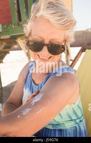 Close up donna senior di applicare una lozione solare mentre in piedi contro la capanna a spiaggia Foto Stock