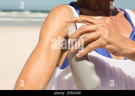Immagine ritagliata della donna di applicare la lozione mentre si sta in piedi in spiaggia sulla giornata di sole Foto Stock
