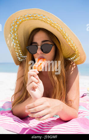 Ritratto di donna di mangiare ghiaccioli mentre vi rilassate in spiaggia sulla giornata di sole Foto Stock