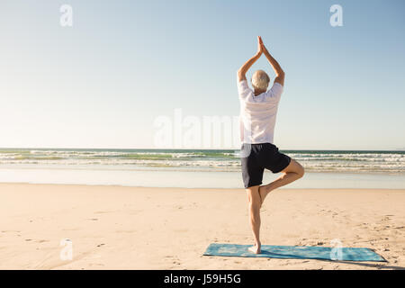 Vista posteriore del senior man praticando la posizione dell'albero a beach Foto Stock