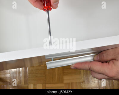 Mani dell'uomo avvitamento di una maniglia in un lato del cassetto Foto Stock