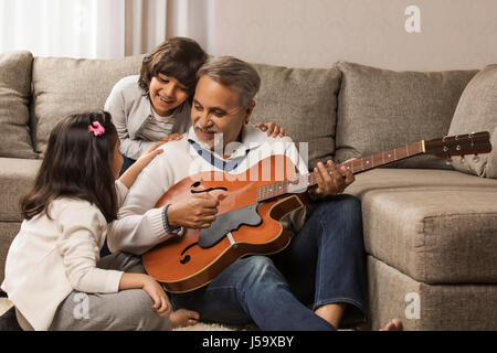 Nonno a suonare la chitarra per i nipoti a casa Foto Stock