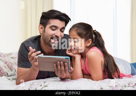 Padre e figlia con tavoletta digitale sul letto Foto Stock