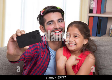 Padre indossa il make-up per divertirsi con la figlia tenendo selfie Foto Stock