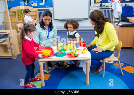 Gli insegnanti giocando con cucina in plastica giocattoli con il loro nido gli studenti in aula. Foto Stock