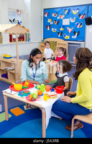 Gli insegnanti giocando con cucina in plastica giocattoli con il loro nido gli studenti in aula. Foto Stock