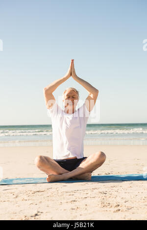 Senior uomo seduto sul tappetino meditando a beach Foto Stock