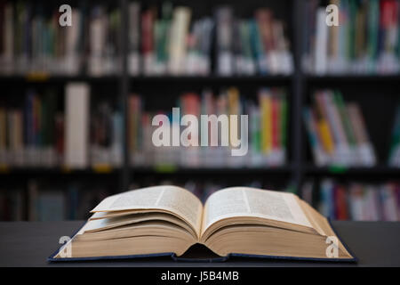 Close up del libro aperto sulla tavola contro la mensola in biblioteca Foto Stock