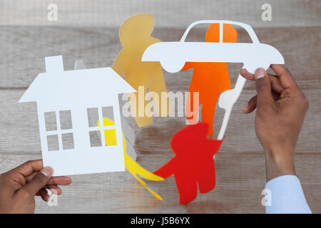 Uomo in possesso di una vettura e una casa in carta contro carta colorata figure da formare sul cerchio nella tabella Foto Stock