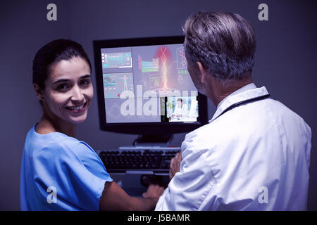 Dottore in uniforme analizzando il corpo umano contro il medico e infermiere esaminando x-ray sul computer Foto Stock