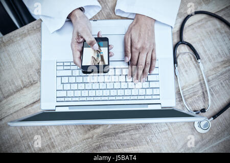 Donna con infortunio al ginocchio contro il medico utilizza lo smartphone sulla scrivania in legno Foto Stock