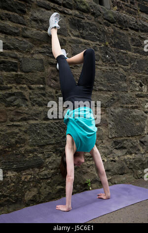 Athletic donna facendo un handstand contro una parete. Azione e uno stile di vita sano concetto. Foto Stock