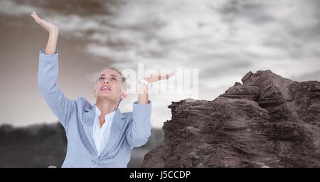 Digital composito di imprenditrice con bracci sollevati dalla rock Foto Stock