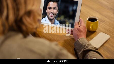 Composito Digitale della vista posteriore della donna le videoconferenze con uomo a tavola Foto Stock