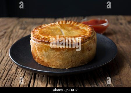 Un britannico tradizionale torta a base di carne seduto su una tavola in legno rustico. Foto Stock