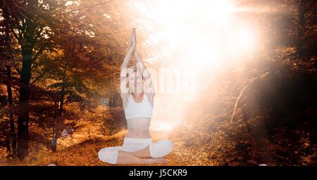 Composito Digitale della doppia esposizione della donna con le mani incrociate a praticare lo yoga nella foresta Foto Stock