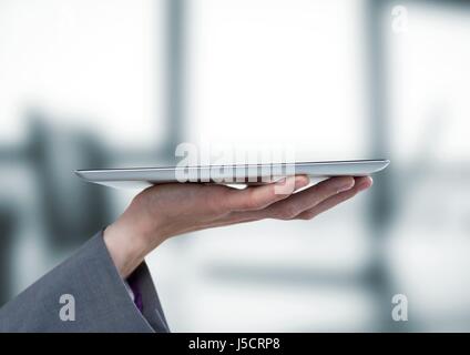 Composito Digitale della mano con la compressa contro sfocate ufficio grigio Foto Stock