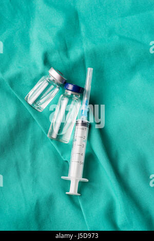Siringa medica e fiale giacente sull'ospedale sfondo verde. Lo sfondo può essere una parte di tessili di un medico o un infermiere uniforme di lavoro Foto Stock
