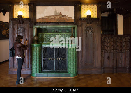 Visitatore utilizza uno smartphone per fotografare la maiolica camino nella ex sala biliardo della Villa Kramář (Kramářova vila) a Praga, nella Repubblica ceca il 13 maggio 2017, tenendo l'opportunità di visitare il sito web di solito chiuso monumenti architettonici durante il festival annuale Open House Praga. La villa progettata dall'architetto austriaco Friedrich Ohmann fu costruito 1911-1914 per uomo politico ceco Karel Kramář e sua moglie russa Nadezhda Kramář, née Khludova. L'edificio è ora servito come residenza ufficiale del Primo Ministro della Repubblica ceca. Foto Stock