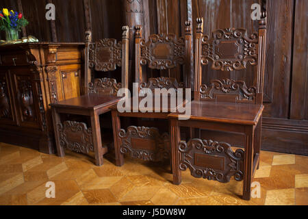 Sedie di legno nella ex sala biliardo della Villa Kramář (Kramářova vila) a Praga, Repubblica Ceca. La villa progettata dall'architetto austriaco Friedrich Ohmann fu costruito 1911-1914 per uomo politico ceco Karel Kramář e sua moglie russa Nadezhda Kramář, née Khludova. La sala biliardo è stata decorata in stile russo. L'edificio è ora servito come residenza ufficiale del Primo Ministro della Repubblica ceca. Foto Stock