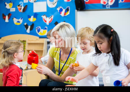 Vivaio insegnante di cucina a giocare il gioco di ruolo con i suoi studenti in aula. Lei è una colata di fingere di tazza di tè per una bambina. Foto Stock