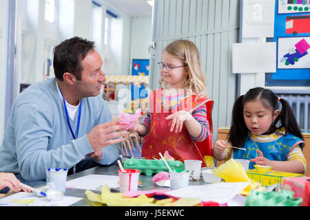 Insegnante maschio parlando con uno del suo vivaio gli studenti in aula. Essi stanno facendo arti e mestieri. Foto Stock