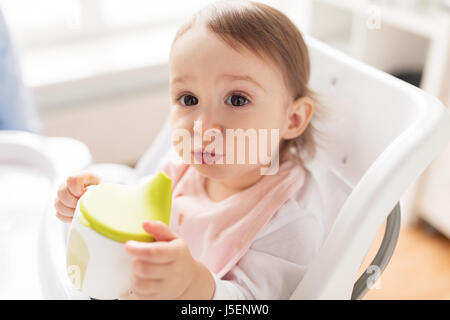 Baby bere dal bicchiere del tubo di lancio nel seggiolone a casa Foto Stock