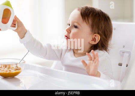 Baby bere dal bicchiere del tubo di lancio nel seggiolone a casa Foto Stock