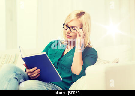 Giovane donna in bicchieri libro di lettura a casa Foto Stock