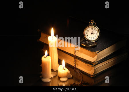 Vintage orologio da tasca su vecchi libri vicino accendendo candele Foto Stock