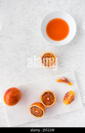 Tutto, dimezzata e spremuta di arance di sangue e succo di frutta fresco su marmo bianco tagliere e white texture di sfondo in marmo con copia spazio. Foto Stock