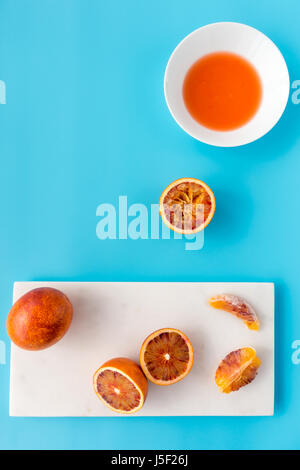 Tutto, dimezzata e spremuta di arance di sangue e succo di frutta fresco su marmo bianco tagliere e solido sfondo blu. Foto Stock