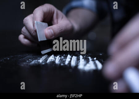 Abile Dope Addict preparando linee di cocaina nel buio Foto Stock