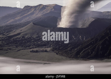 Vista mozzafiato del volatile e scoppiando Gunung Bromo con la nube di cenere produca del cratere e tutta l'area coperta in scuro cenere vulcanica Foto Stock