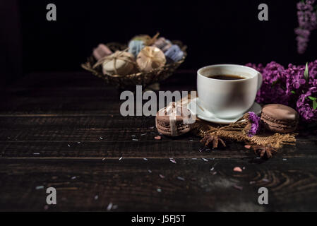 Tazza di caffè sul tovagliolo di lino e diversi macarons nella treccia vaso con ramo di lilla. Foto Stock