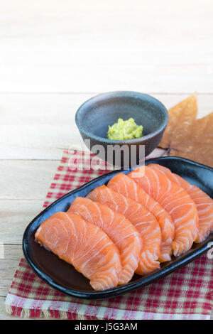 Fette di Salmone crudo sulla piastra nera con uno sfondo di legno Foto Stock