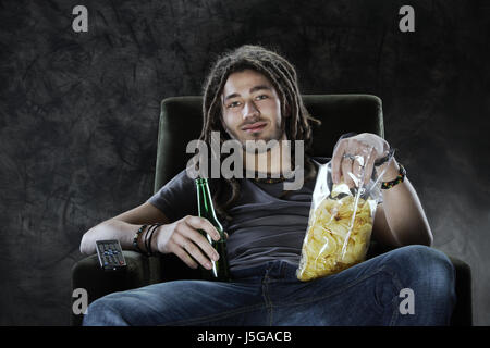 Giovane uomo guardando la televisione mangiare patatine e bere birra Foto Stock